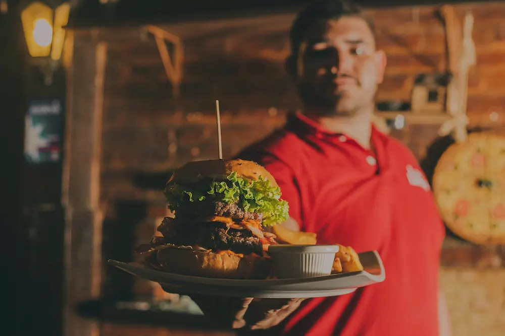 Image of a waiter holding out a plate with a burger in a small restaurant for sale in Canada
